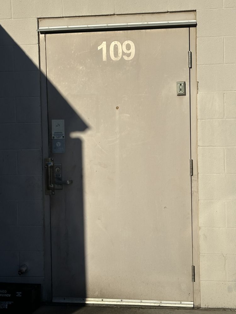 Gray door labeled “109” in a sunlit exterior wall with deep shadow on the left.