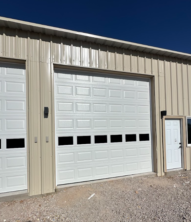 Beige metal garage building with two white overhead doors and a side entry door under a blue sky