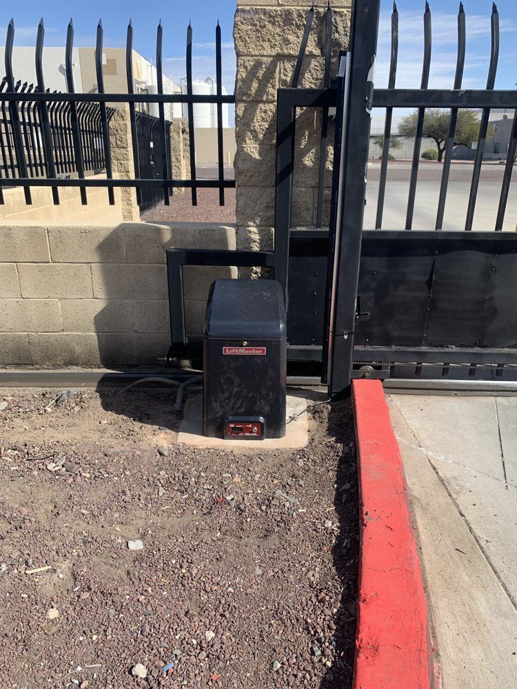 Black utility box beside a sidewalk and metal fence, with desert landscape in the background.