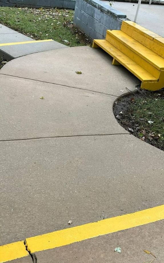 Concrete sidewalk ramp with yellow painted edges and steps beside a grassy area