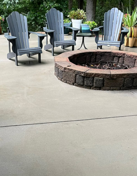 Patio with three blue Adirondack chairs around a stone fire pit on a concrete surface