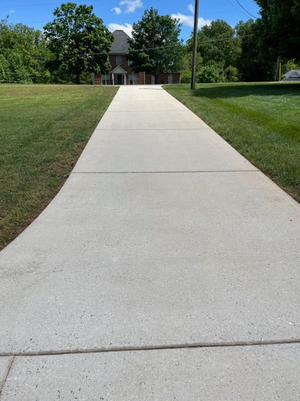 Concrete sidewalk leading to a building across a grassy lawn under a blue sky