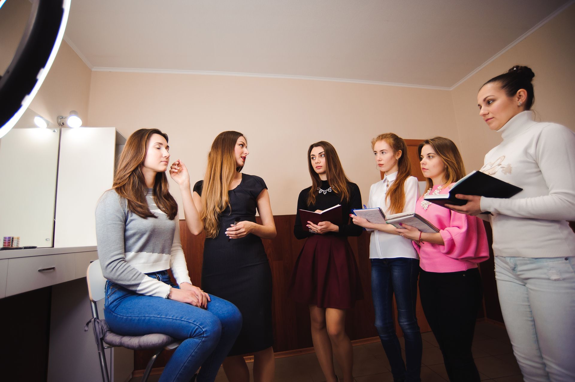 A group of women are standing around a woman sitting on a stool.