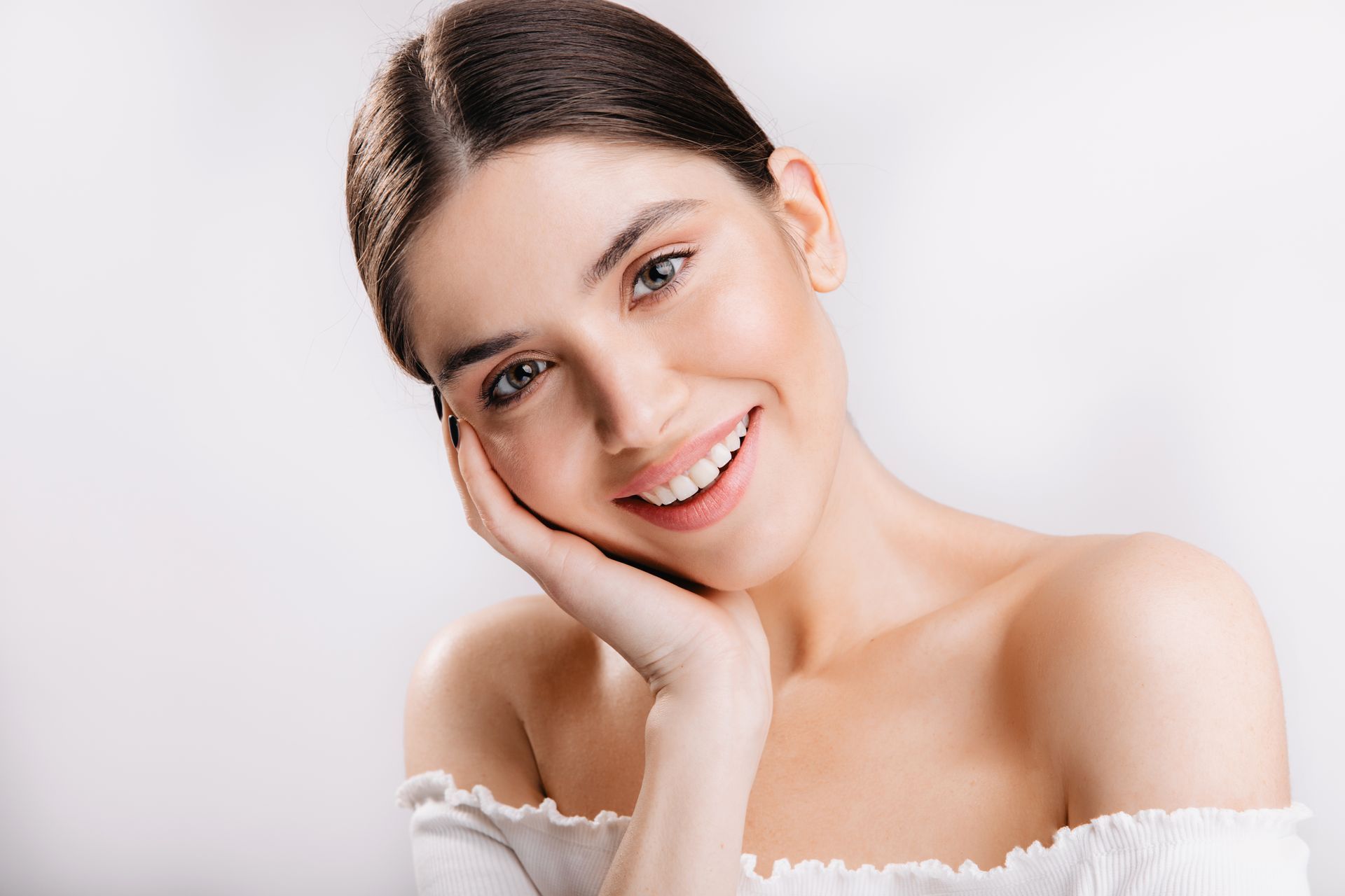 A woman is smiling and touching her face with her hand.