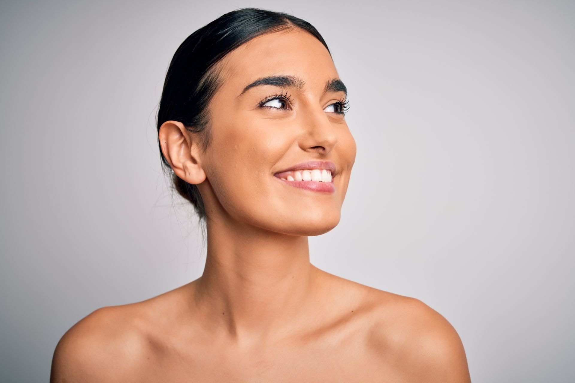 A woman without a shirt is smiling and looking up at the sky.