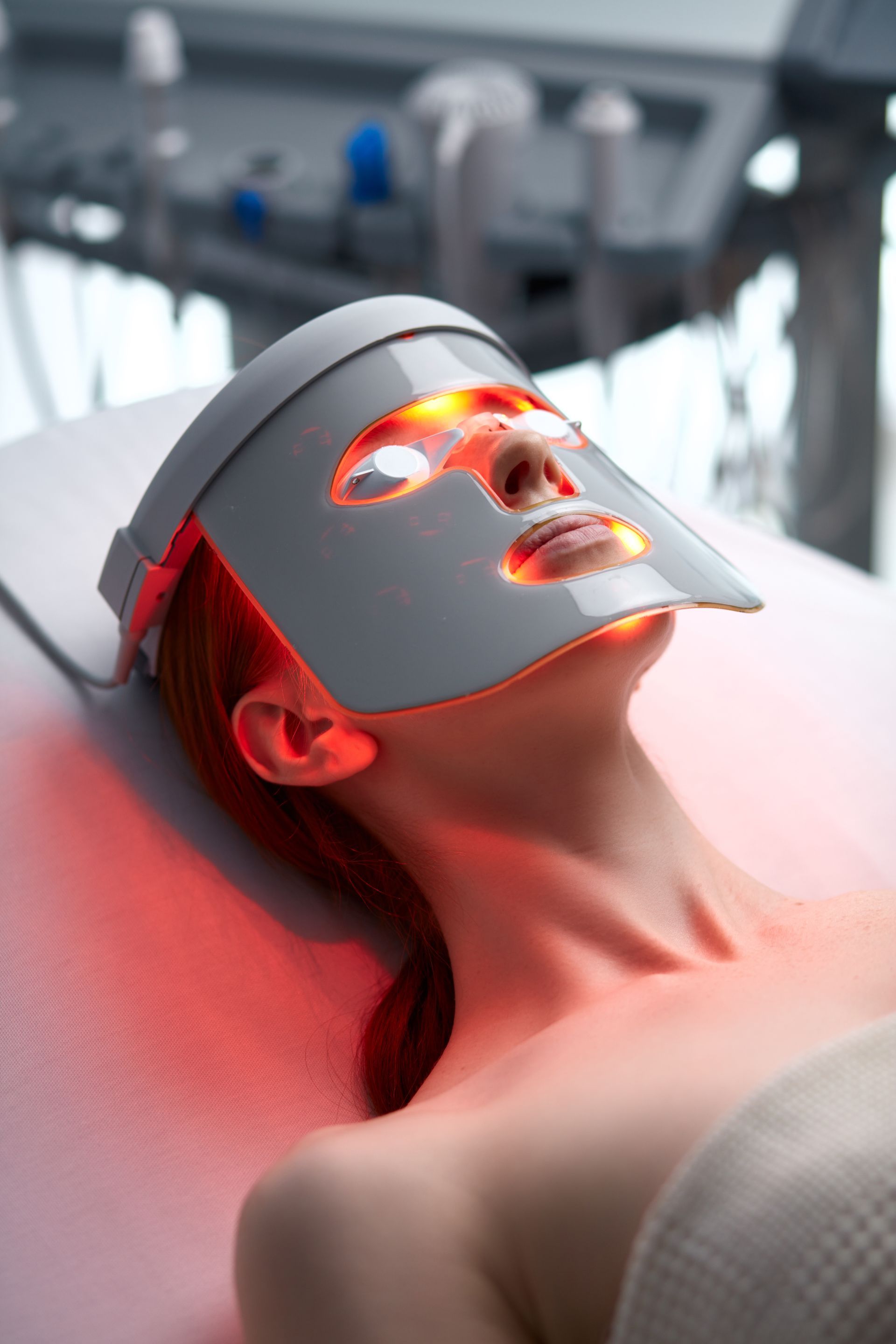A woman is laying on a bed with a led mask on her face.