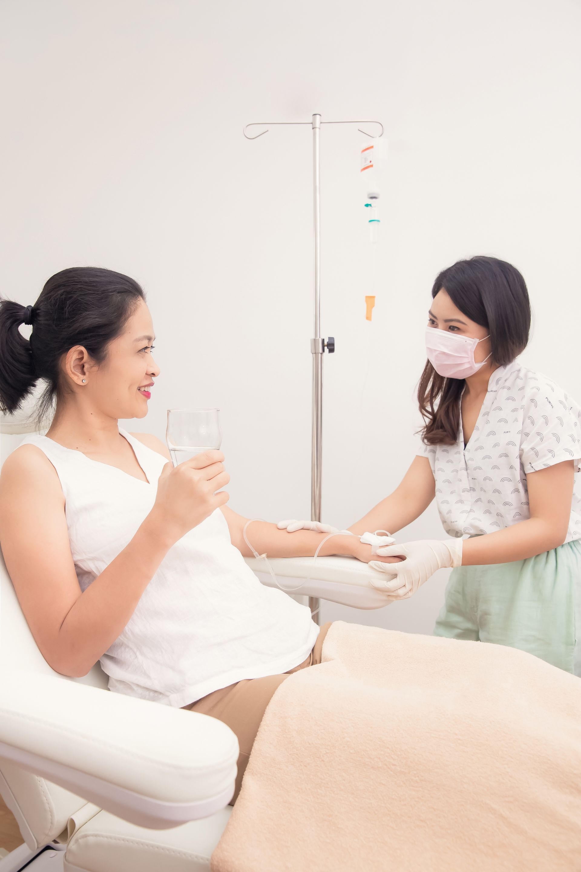 Woman receiving IV fluids in medical setting; nurse attending.