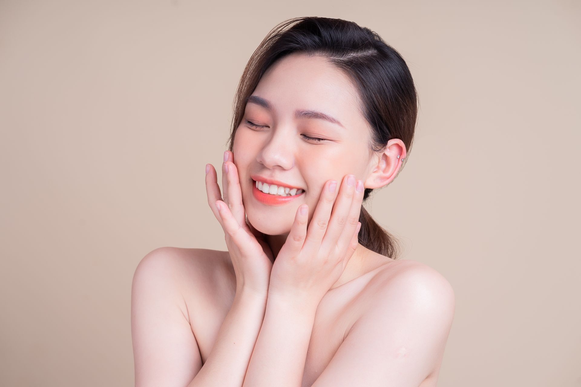 A woman is smiling and touching her face with her hands.