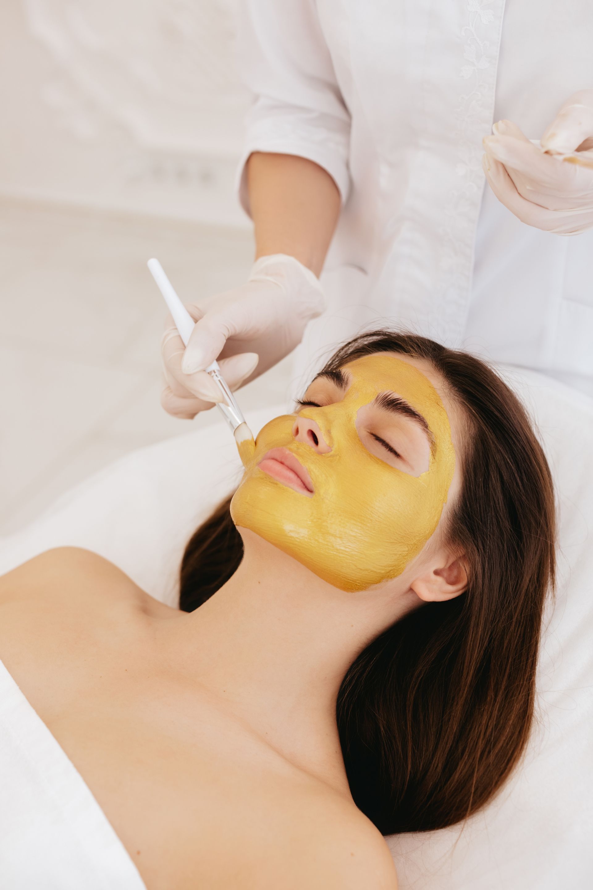 A woman is smiling while applying cream to her face.