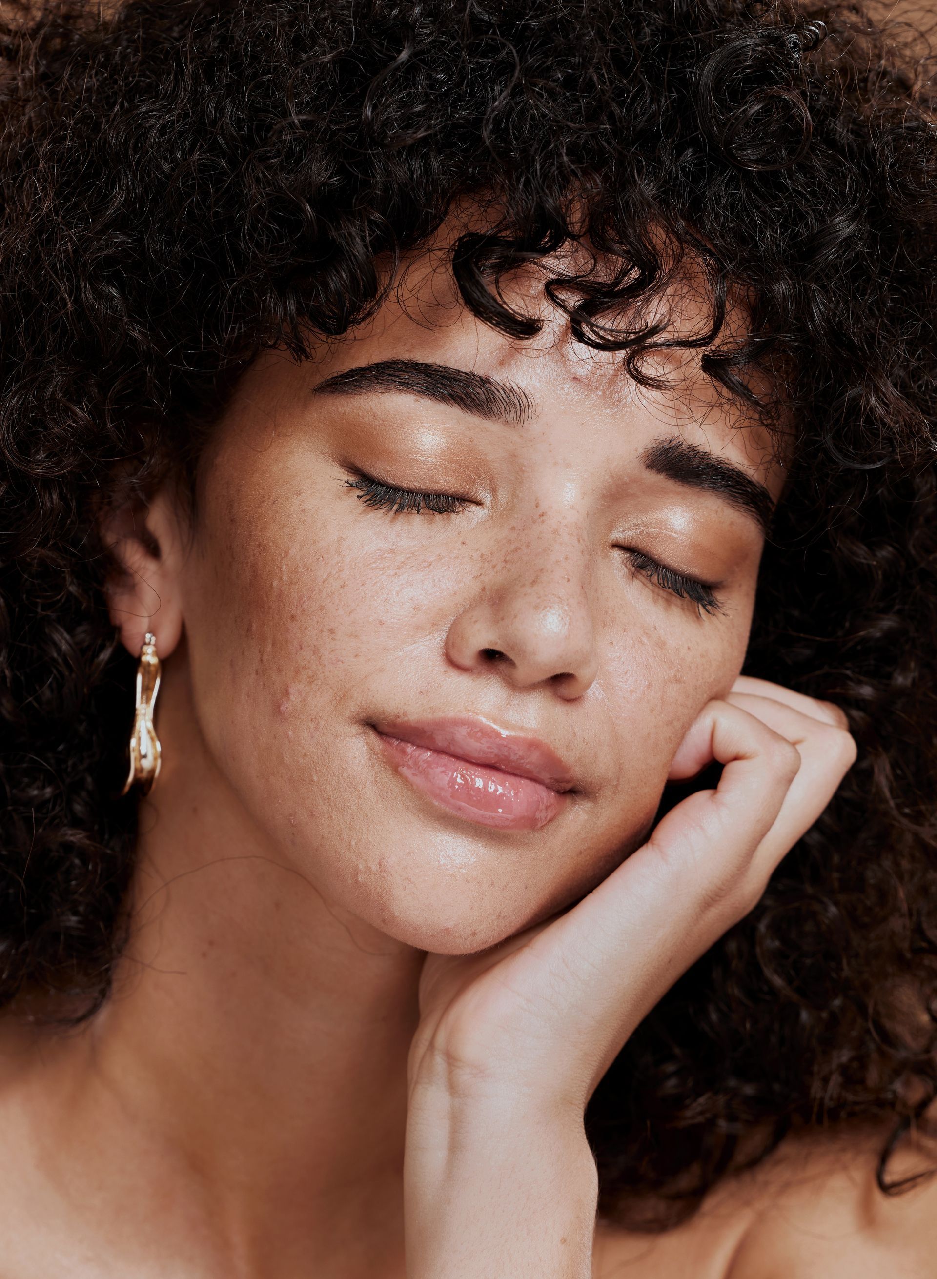 Woman with curly dark hair, closed eyes, and hand under her chin, in soft focus.