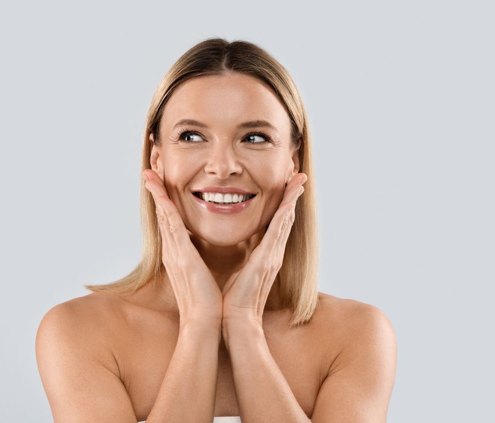 A woman is smiling and touching her face with her hands.