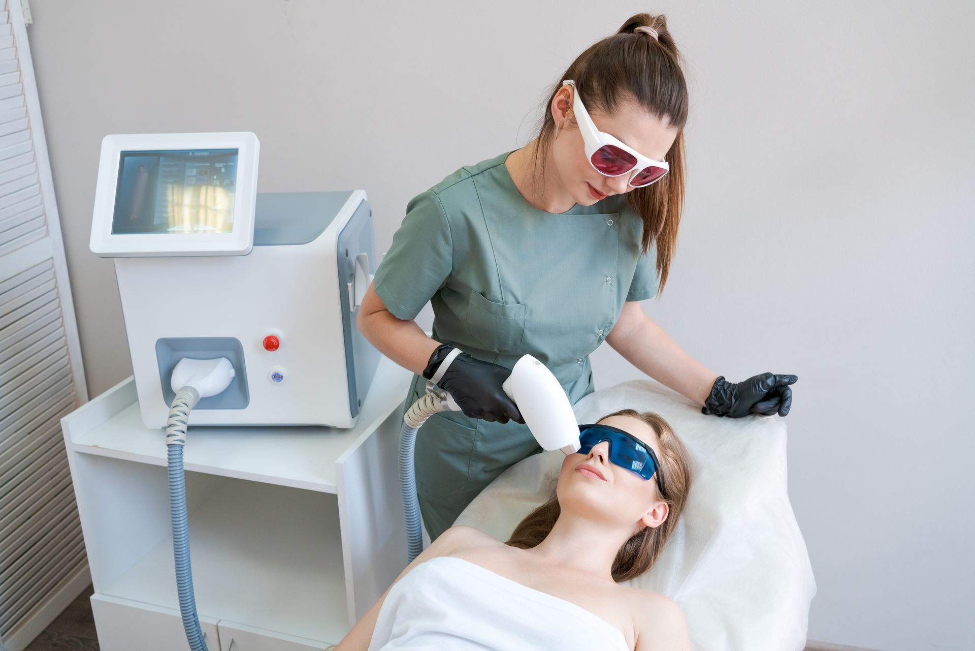 Esthetician using a handheld laser device on a client in a treatment room