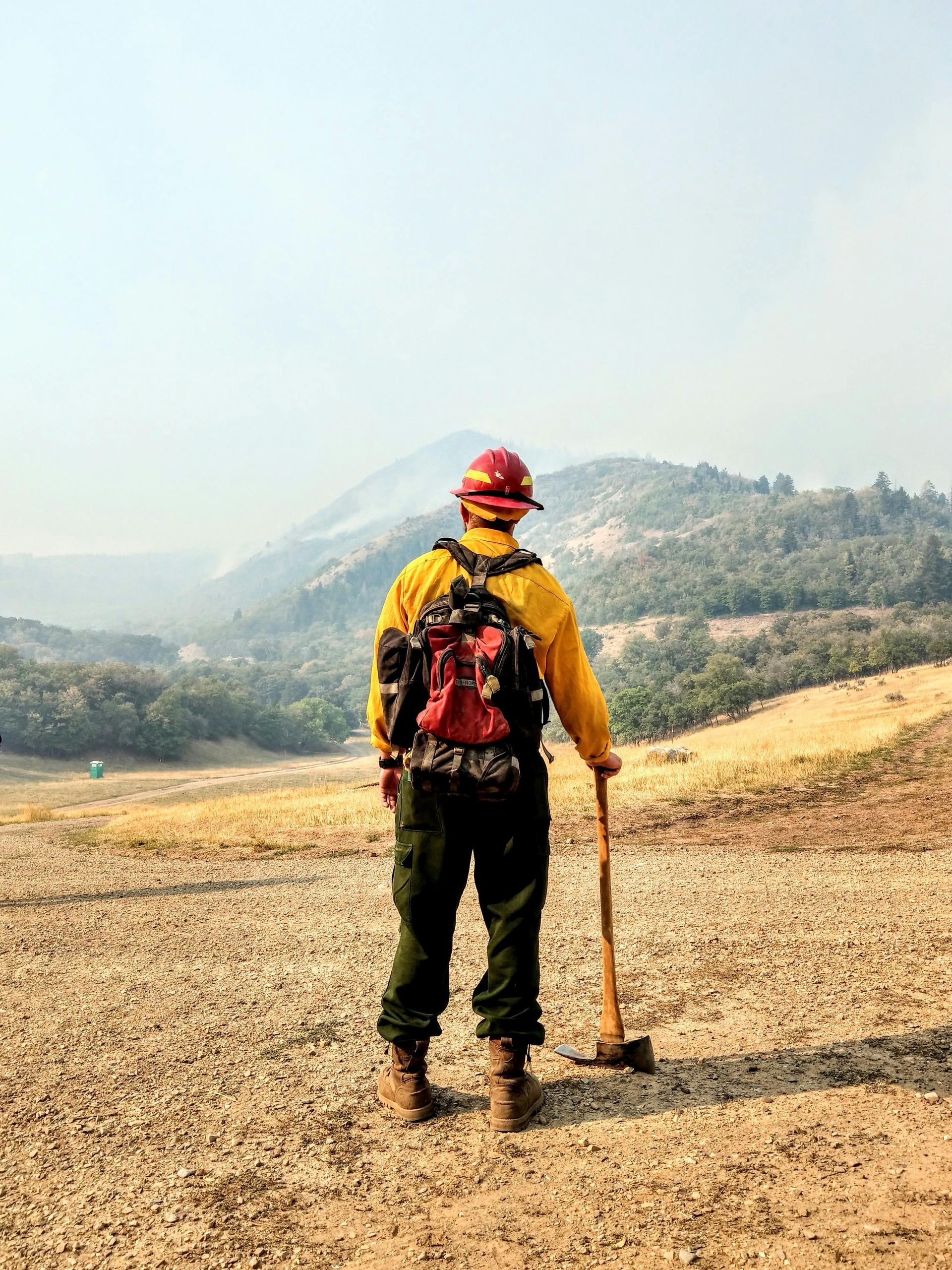 A firefighter is standing in the middle of a field holding a shovel.