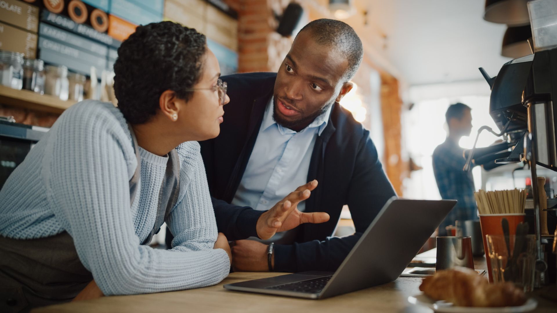 Two small business owners in their cafe having a discussion with an open laptop computer.