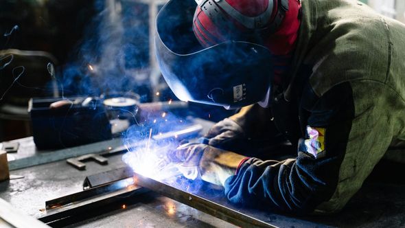 Welder in protective gear welding metal frame, sparks flying.