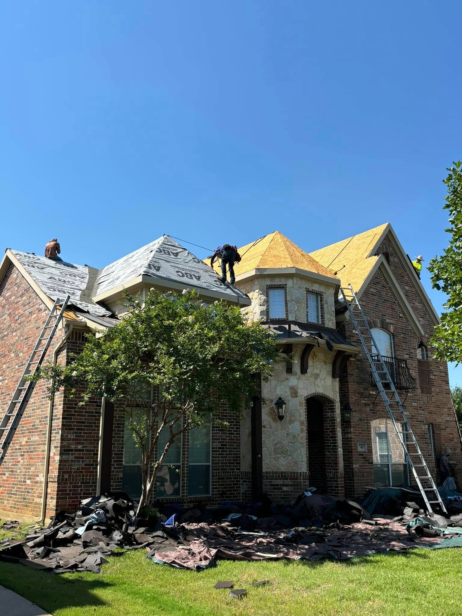 Roofers working on a house under a clear blue sky; debris and ladders present.
