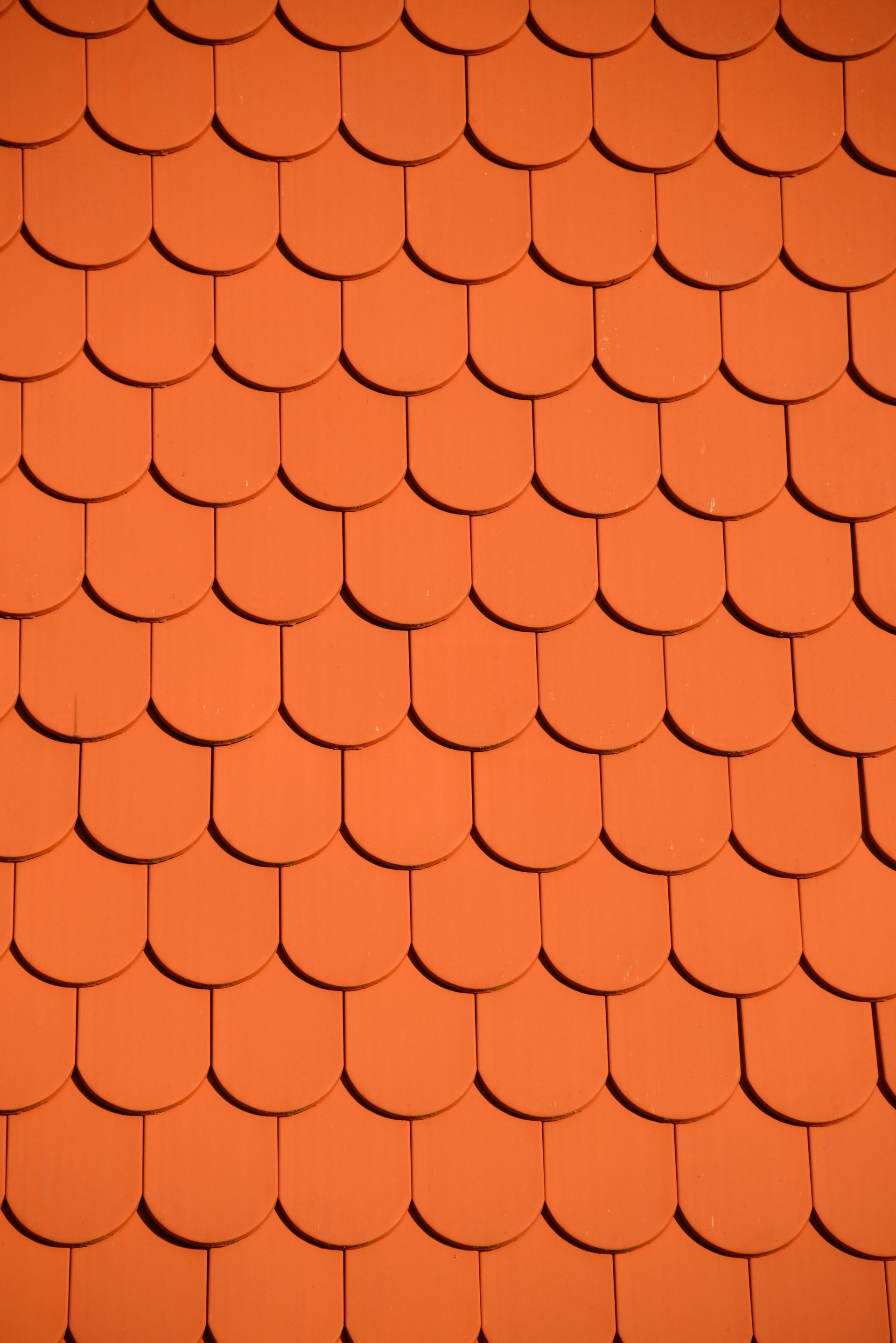 Orange, scallop-shaped roof tiles, overlapping in a grid pattern, casting shadows.