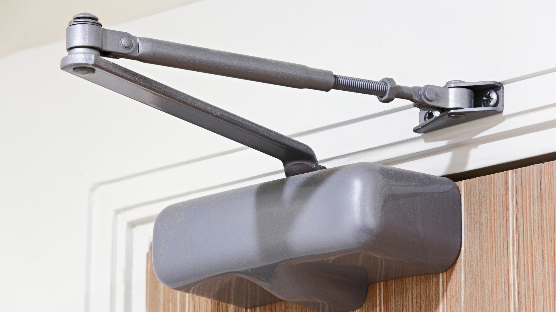 A close up of a door closer on a wooden door.