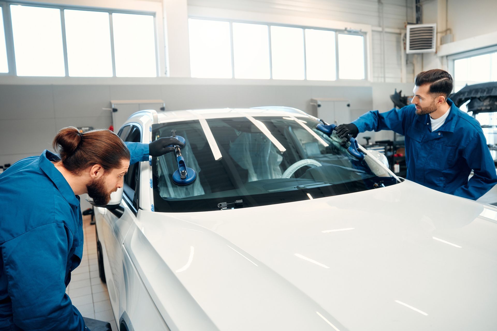 Two mechanics change a windshield on a car in a car workshop.