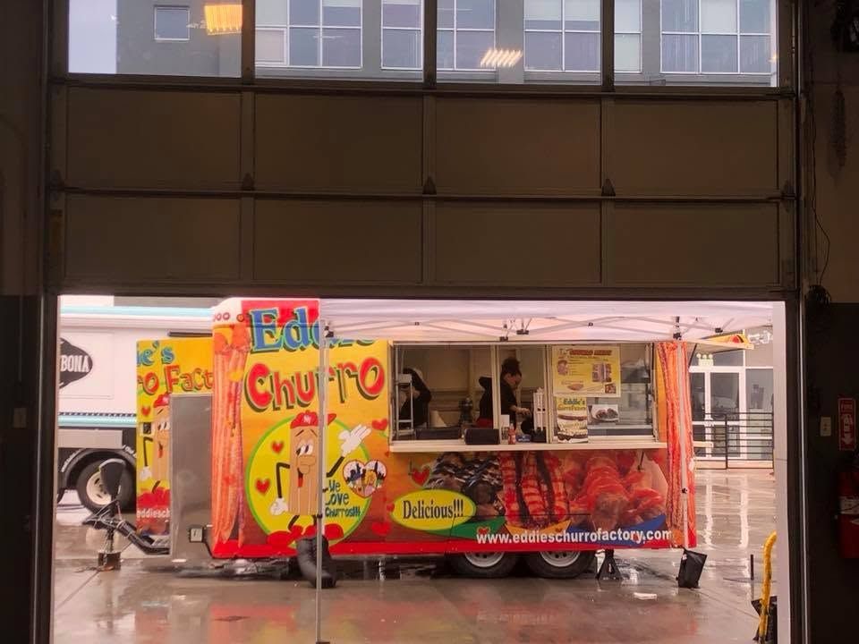 Red and yellow food cart labeled “Eat Churro” in a garage doorway, with a bicycle inside.