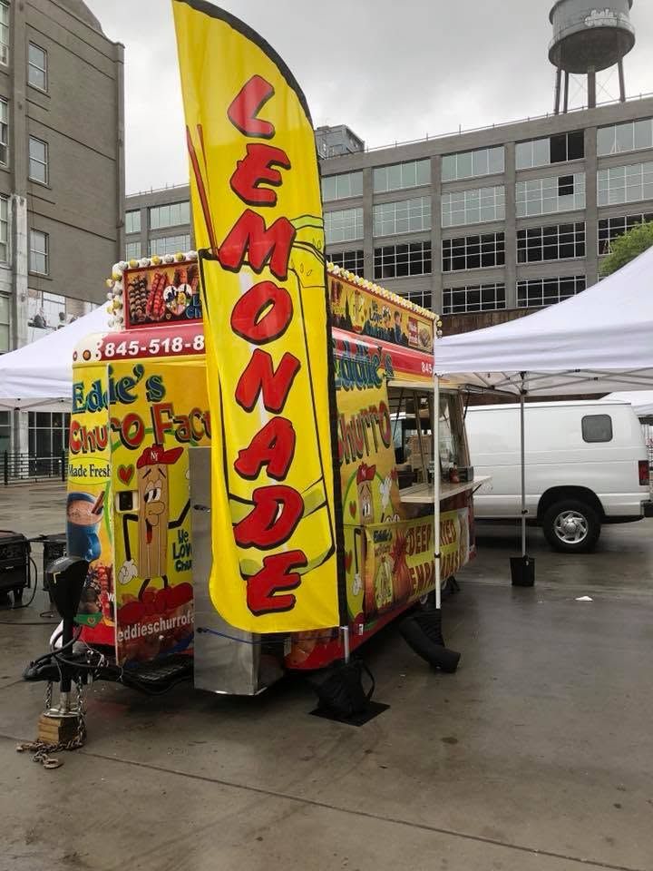 Bright yellow lemonade food truck with red lettering at an outdoor market on a rainy day