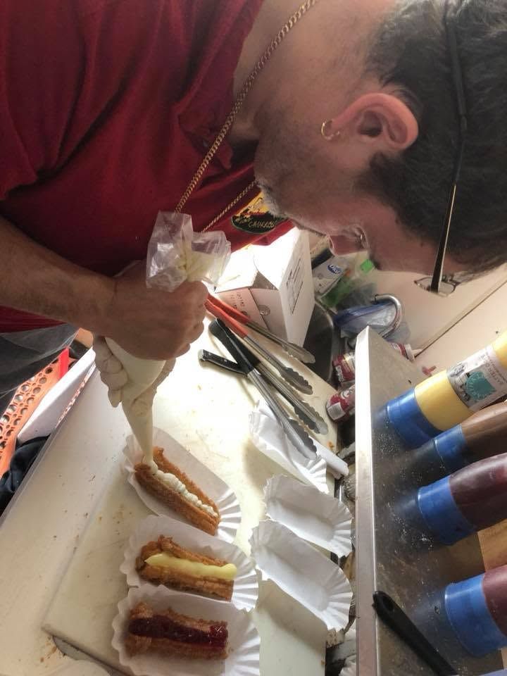 Person piping filling onto pastries on a tray at a kitchen counter