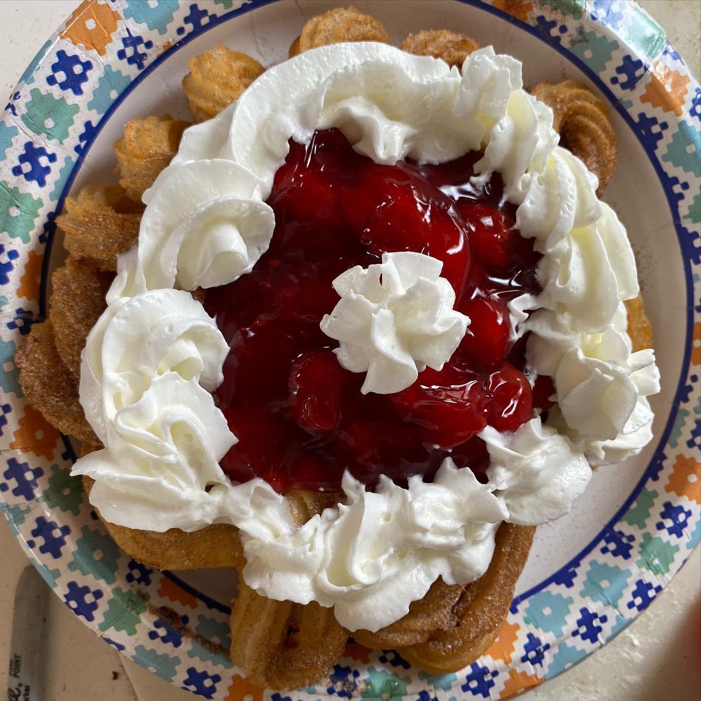 Dessert topped with whipped cream and red strawberry sauce on a floral plate
