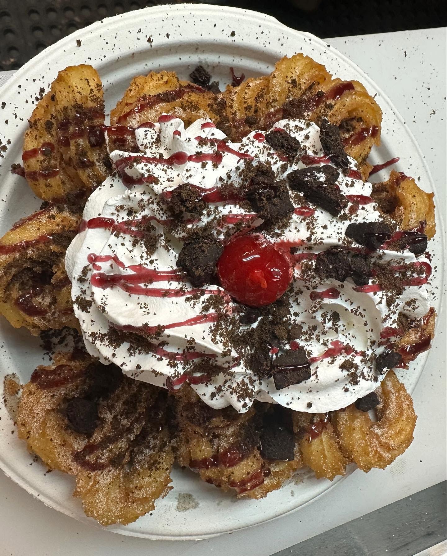 Dessert plate with whipped cream, chocolate drizzle, cherry, and sliced fruit around the edge
