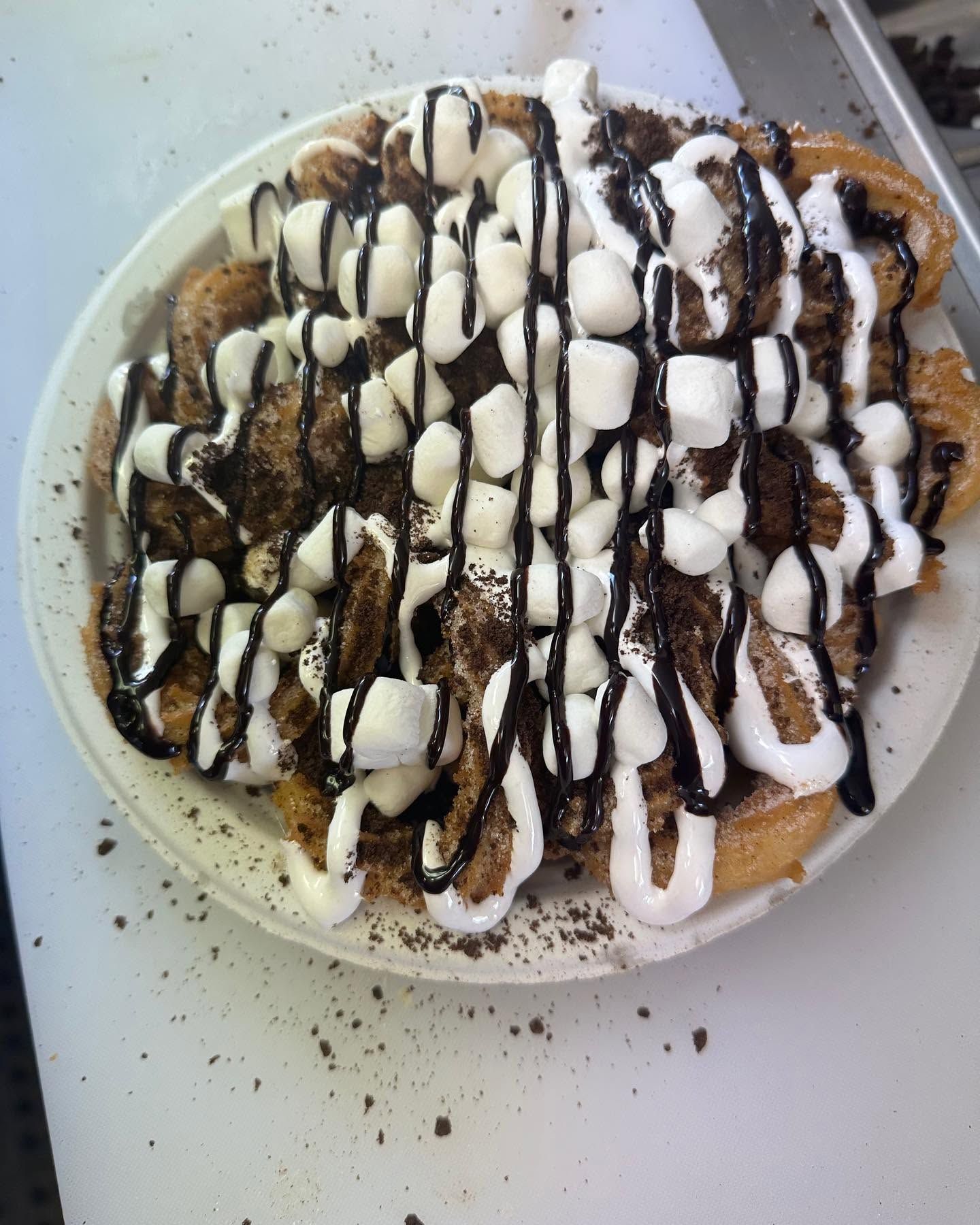 Plate of dessert drizzled with white icing and chocolate sauce, topped with crushed nuts and powdered sugar