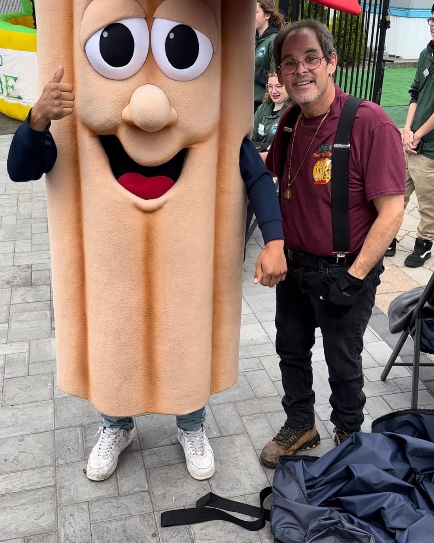 Person beside a smiling hot dog mascot at an outdoor event