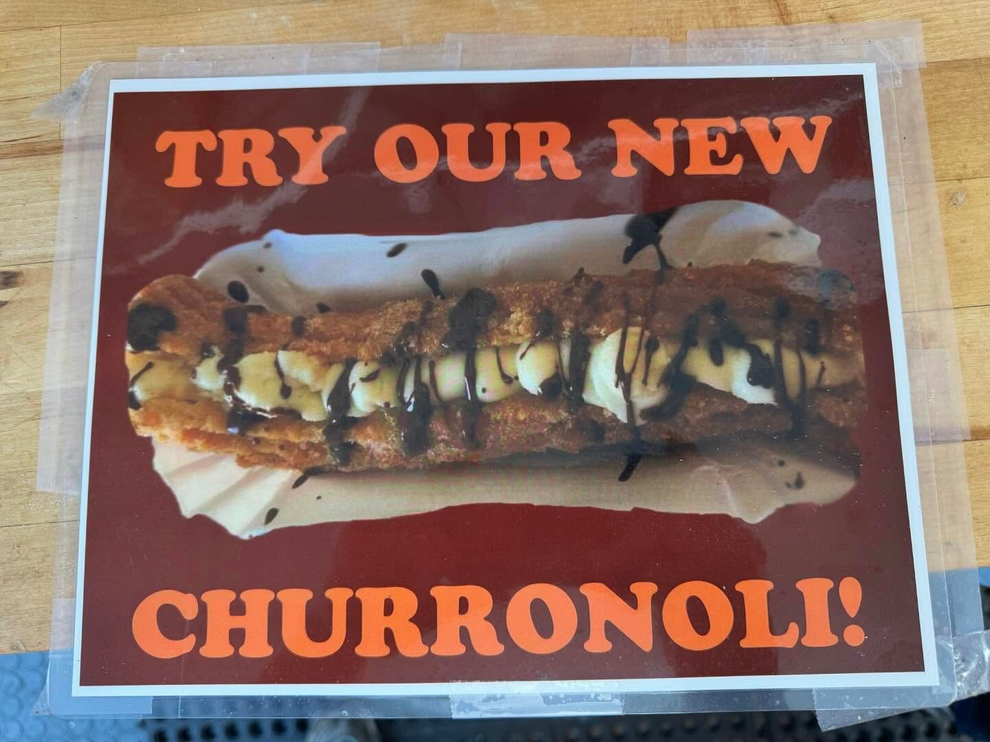 Sign advertising “TRY OUR NEW CHURRONOLI!” with a chocolate-drizzled dessert on a red background