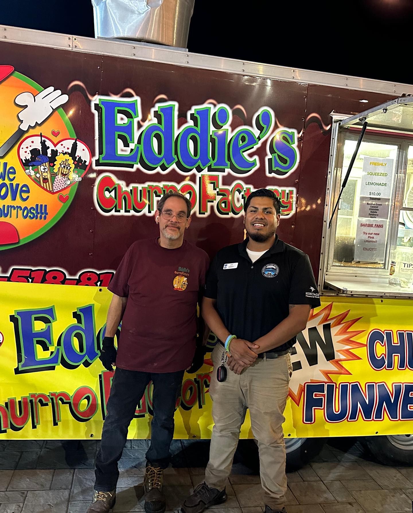 Two men standing in front of an Eddie’s Churro cart with colorful signage.