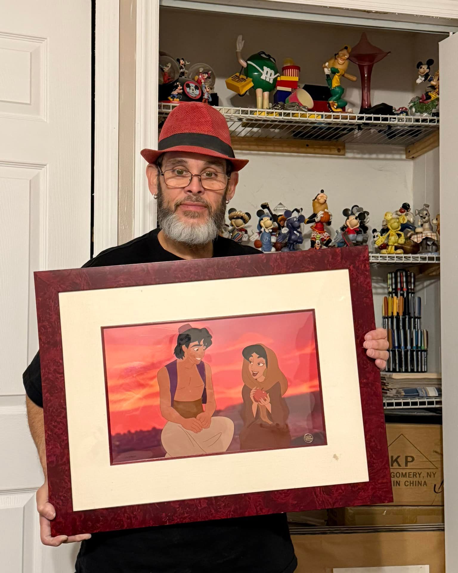 Man holding a framed sunset artwork in a room with shelves of figurines