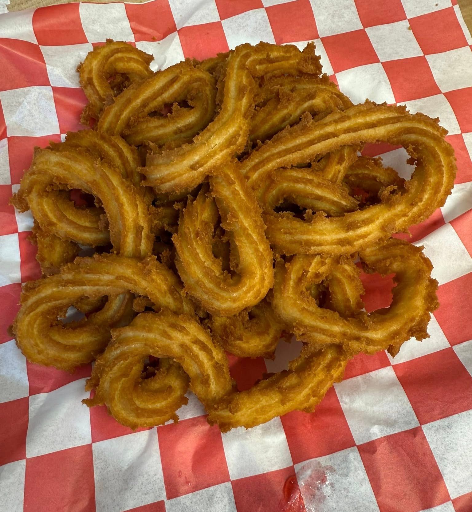 Pile of golden fried churros on red-and-white checkered paper