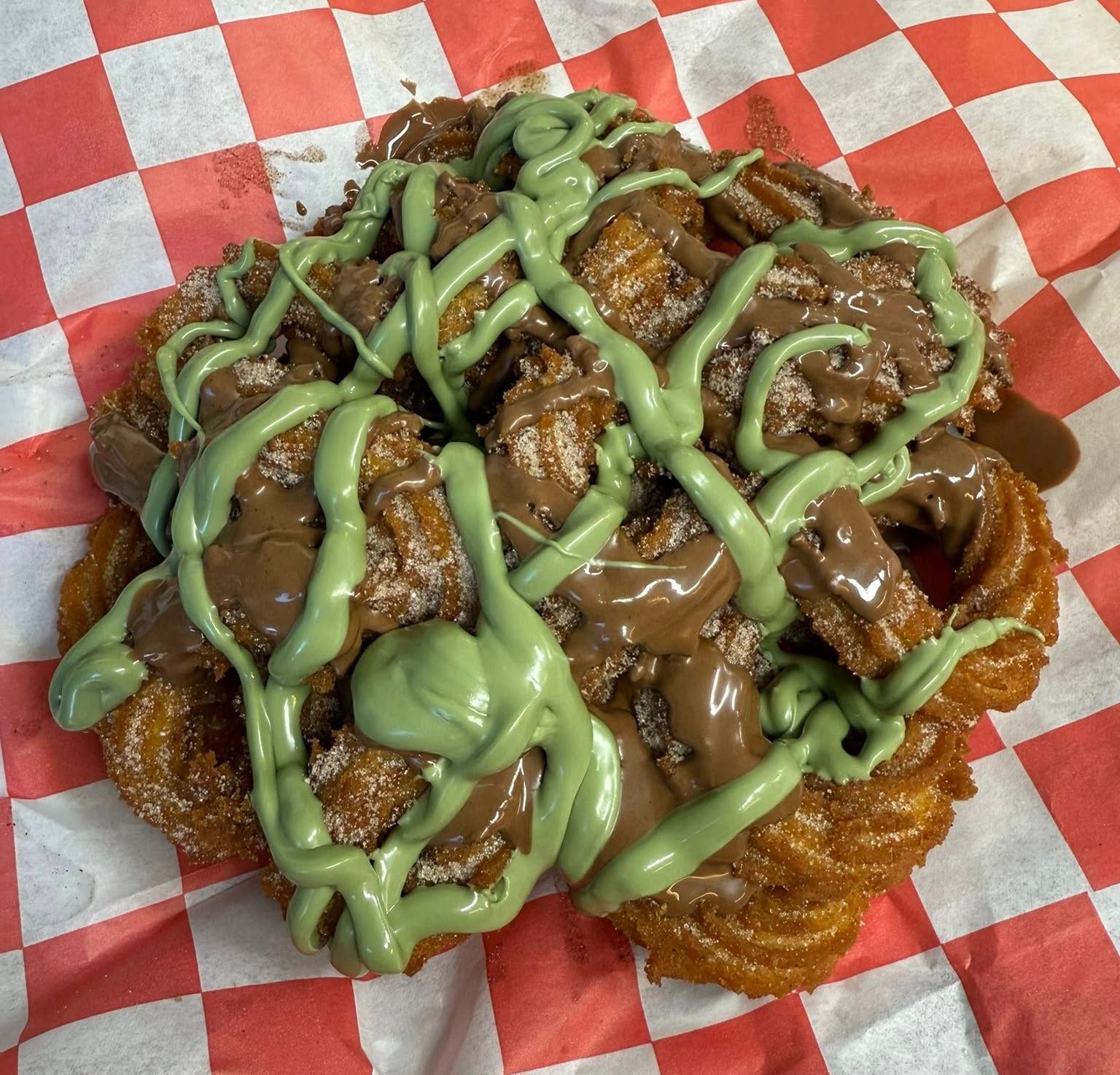 Fried pastry topped with chopped nuts, brown sauce, and green icing on red-checkered paper.