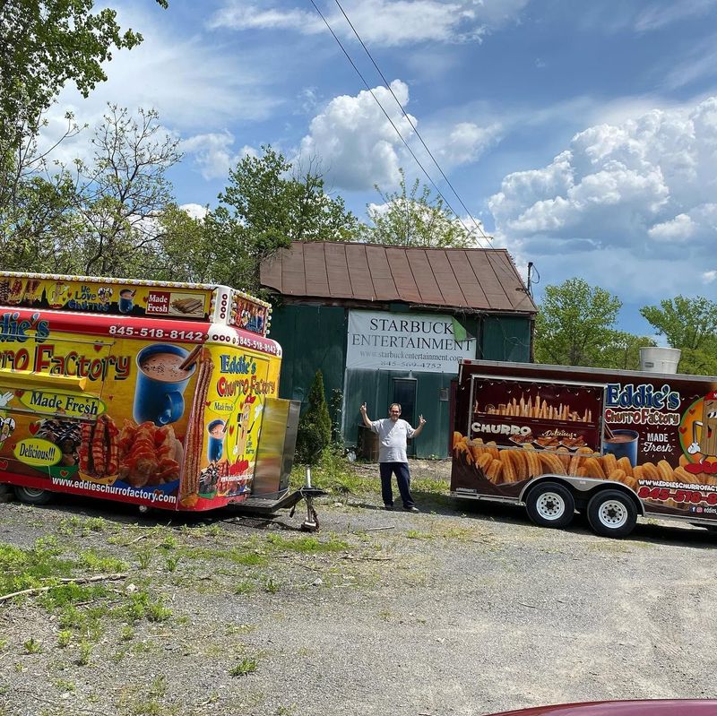 Two colorful food trailers parked by a small building under a cloudy sky, with a person standing in front.