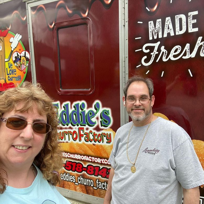 Two people posing in front of a red food truck with “Made Fresh” and “Eddie’s” signage