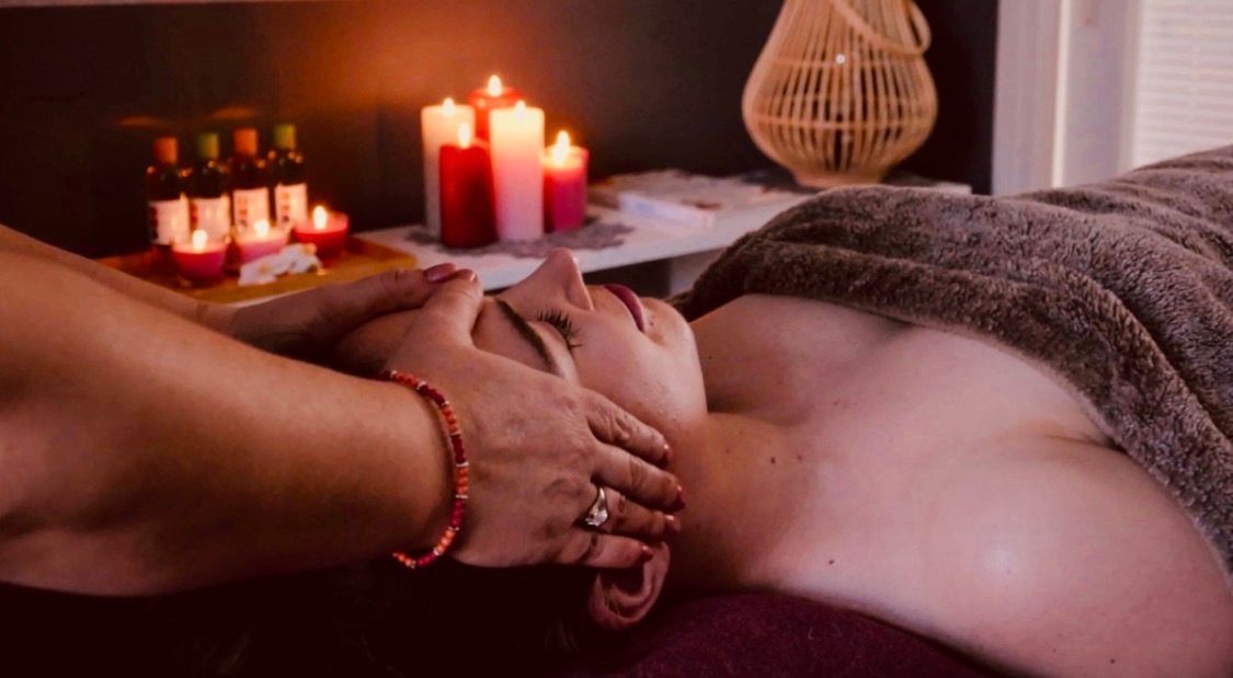 Spa-massage met kaarsen; iemand krijgt een gezichtsmassage op een tafel in een schemerige, ontspannende ruimte.