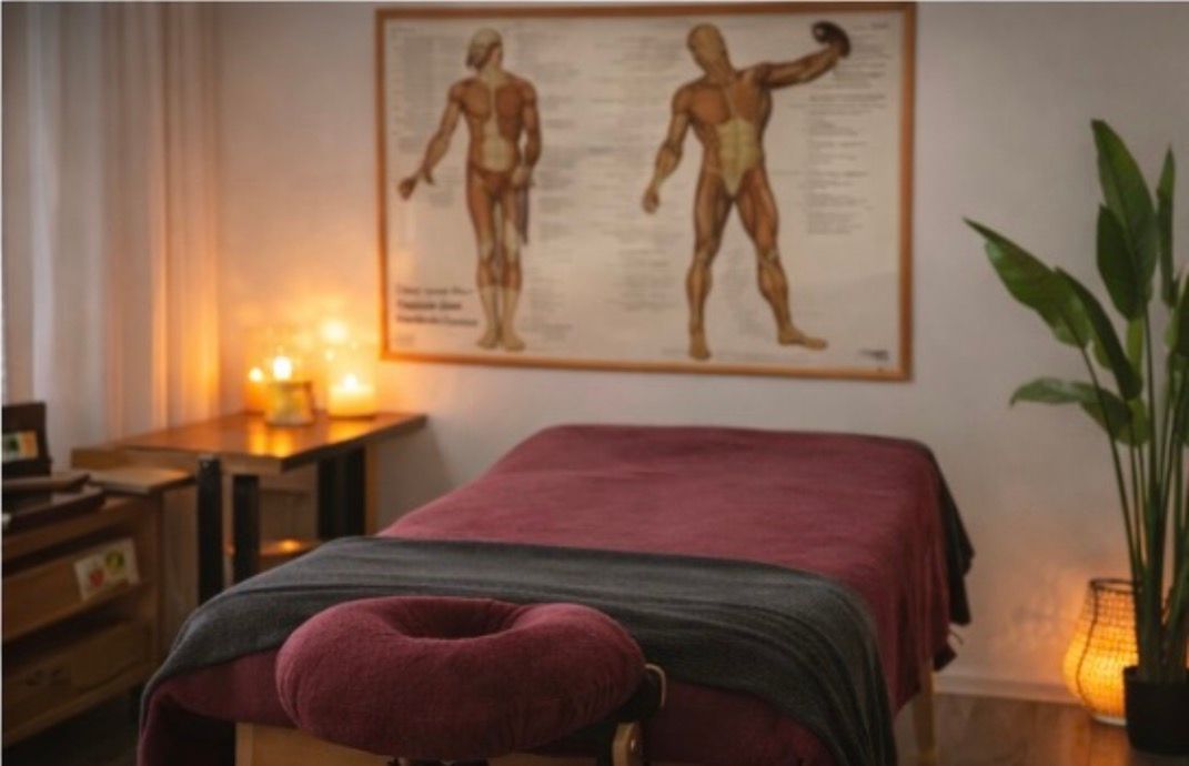 Massageruimte met een behandeltafel, anatomische muurdecoratie, kaarsen en sfeervolle verlichting.