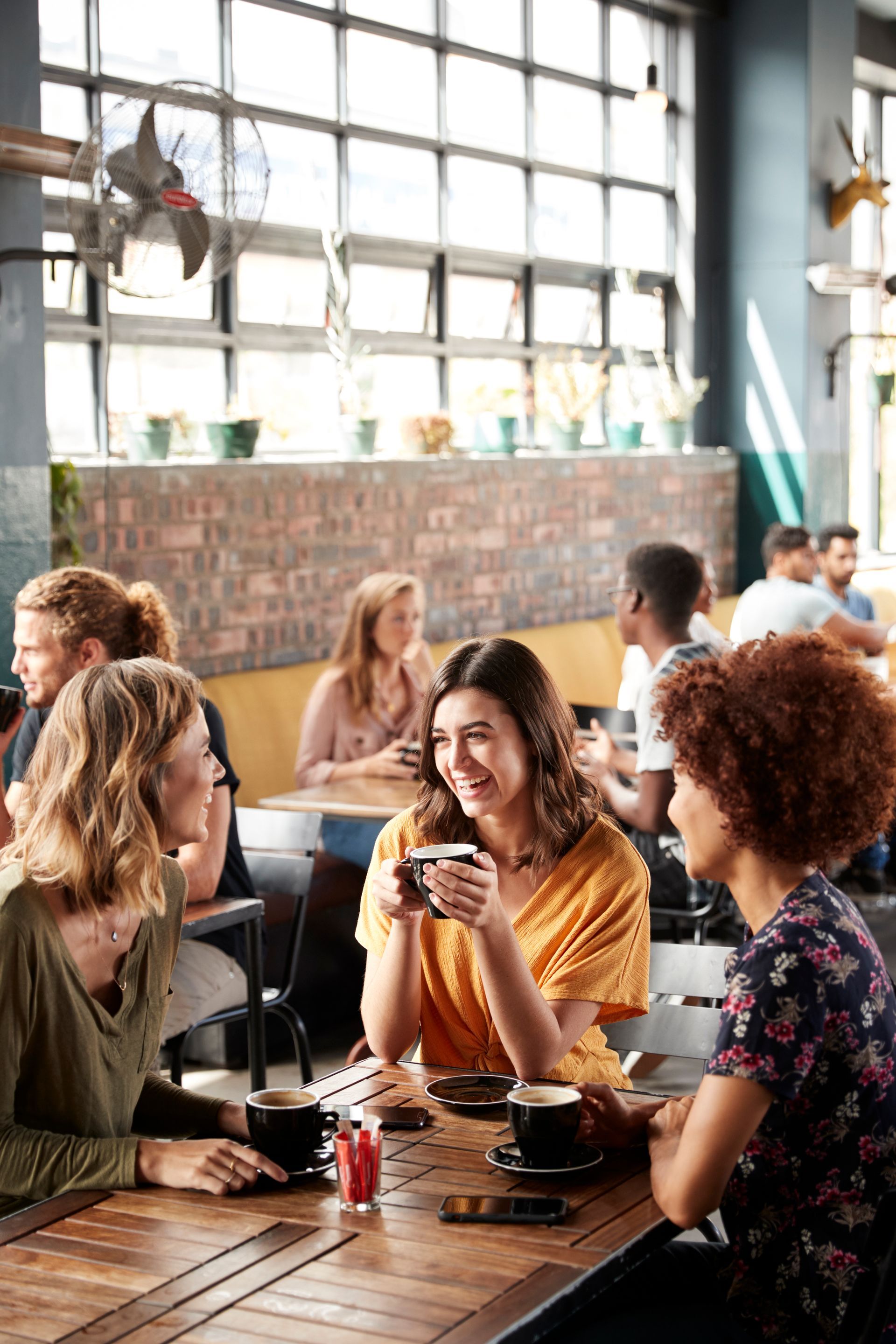 People chatting and eating at a lively café with large windows and warm natural light