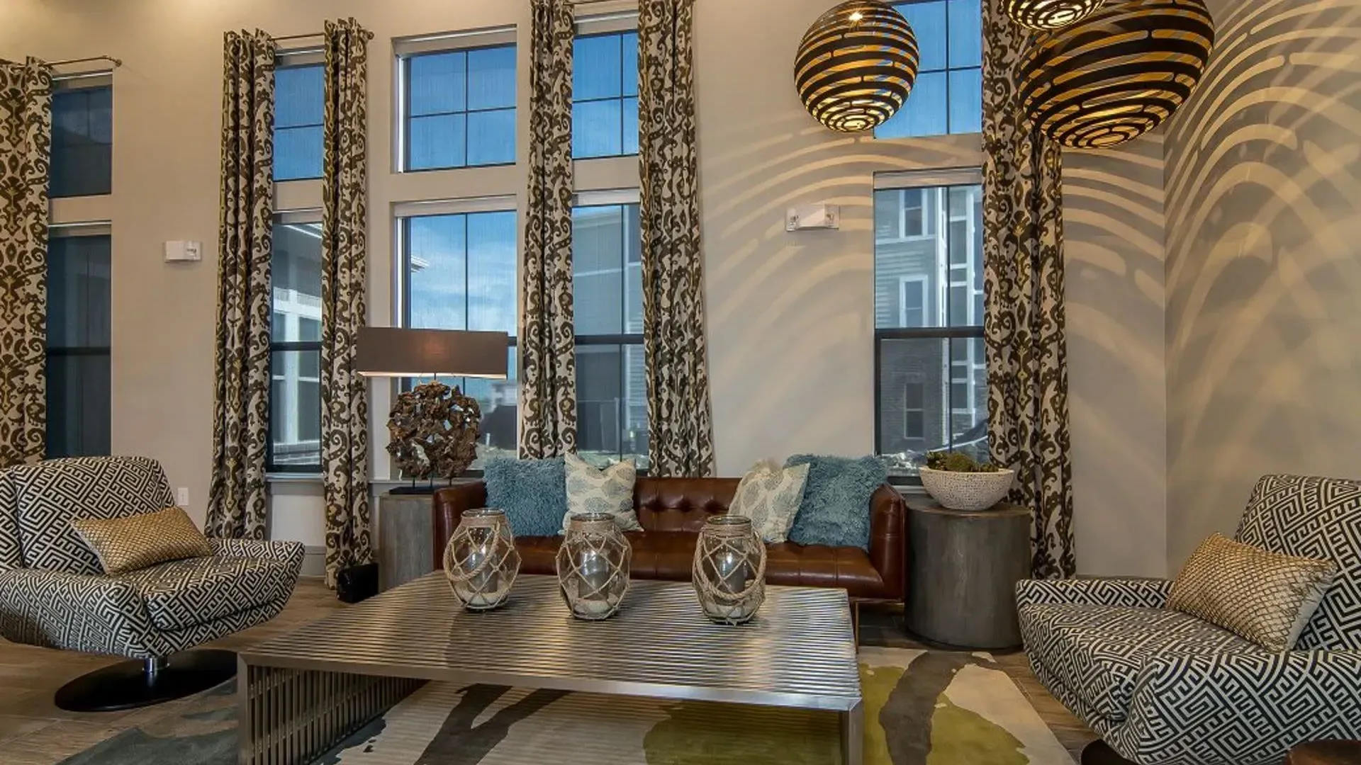 Modern community lounge with patterned chairs, a leather sofa, and large windows.