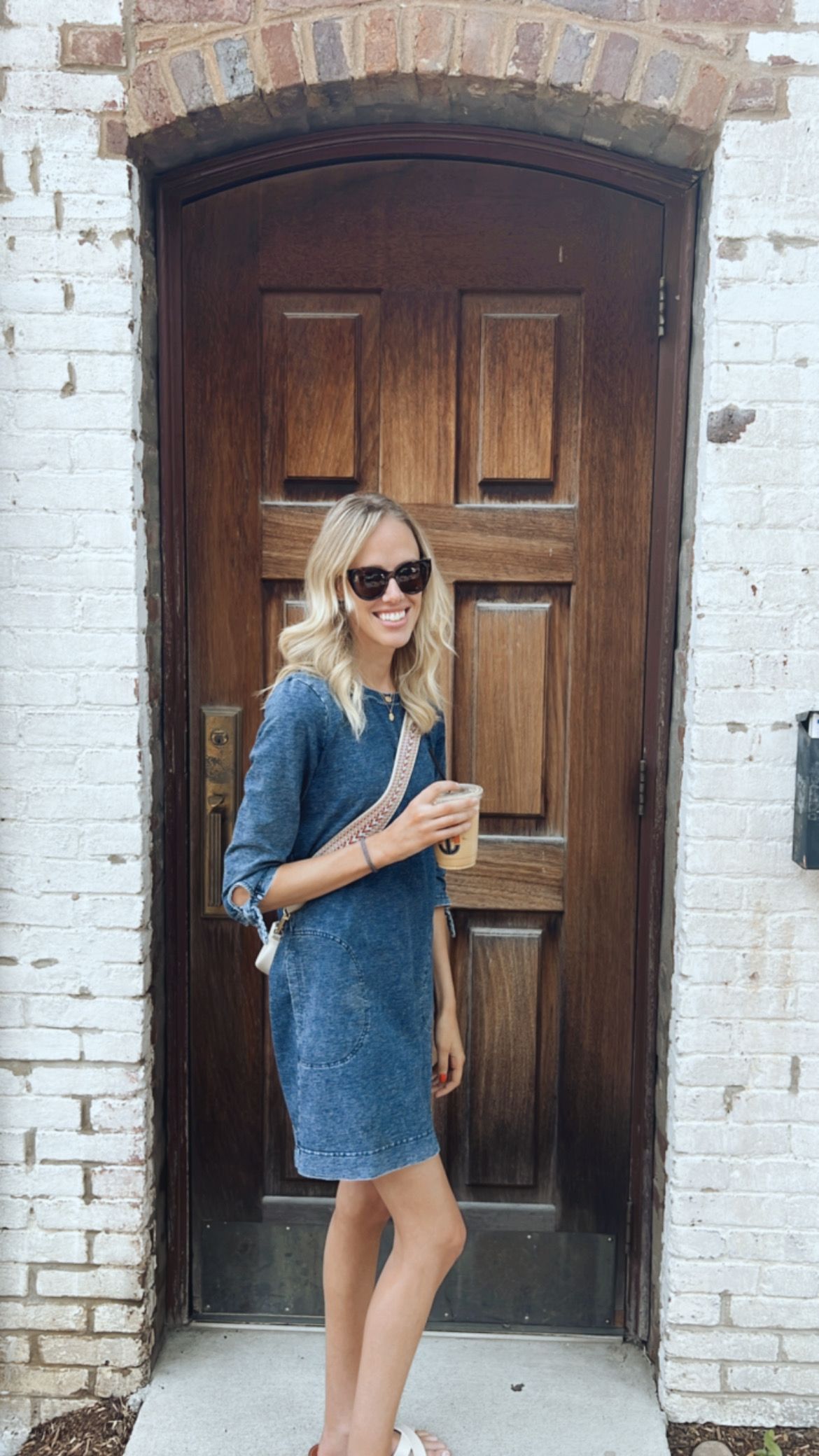Woman in a blue dress and sunglasses standing in front of a wooden door.