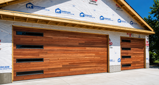 Modern house exterior with unfinished wood garage doors and white wrap under construction