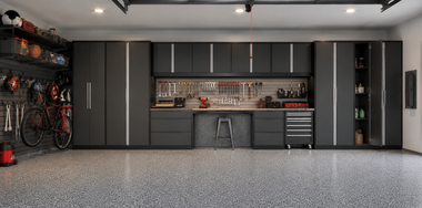 Modern garage with dark cabinets, tool benches, bikes on the left, and a speckled gray floor.