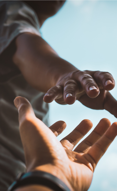 Two hands reaching toward each other against a bright blue sky