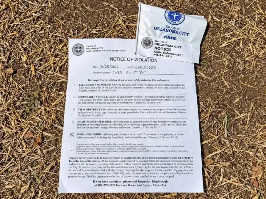 Oklahoma City code enforcement notice of violation for junk and debris posted with a city flag on dry ground