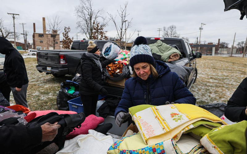 Volunteers distribute warm blankets from a truck on a cold day, helping those in need in a community park setting.