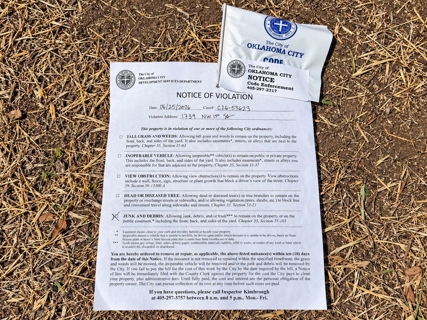 Oklahoma City code enforcement notice of violation for junk and debris posted with a city flag on dry ground