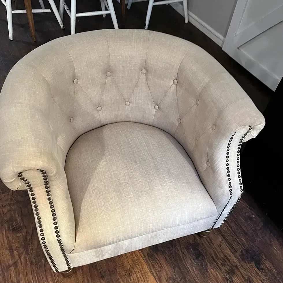 Beige upholstered barrel chair with button tufting and studded trim.