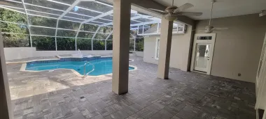 Covered patio overlooking an empty screened-in pool with beige columns and tiled floor